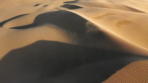 4K cinematic aerial of strong wind blowing the golden sand from dunes at sunset Stock Footage