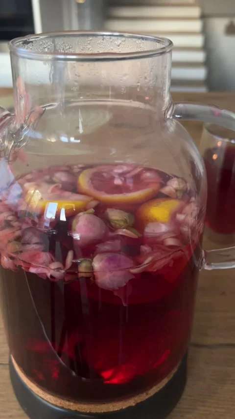 4K Close Up Brewed Red Winter Fruit Tea Floating Rosebuds Glass Teapot B-Roll⁠ Video stock 347099043