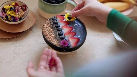 4K Close-up Hand Placing Yellow Flower Garnish on Coconut Smoothie Bowl Stock Footage 330479460