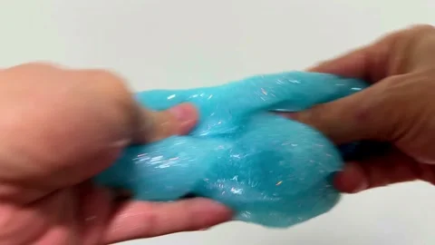 4K close-up of a hand playing with blue glittery slime on a white background Stock Footage 288688476
