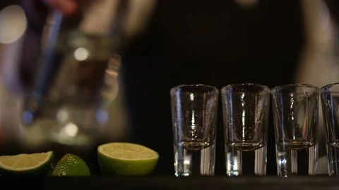 4K Close Up On Hands Of Barman Pouring Liquor Into Row Of Shot Glasses Stock Footage 75628020