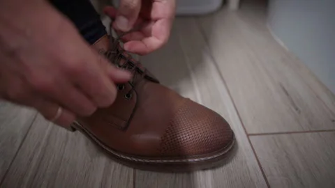 4K close-up of man lacing classic brown leather shoes before work in stylish int Video stock 318990950