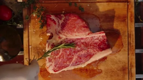 4K Close-up Raw T-Bone Steak Seasoned Salt Herbs Wooden Cutting Board Stock Footage 330480827