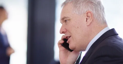 4K Close up of serious grey haired businessman talking on phone in the office Stock Footage 104153771