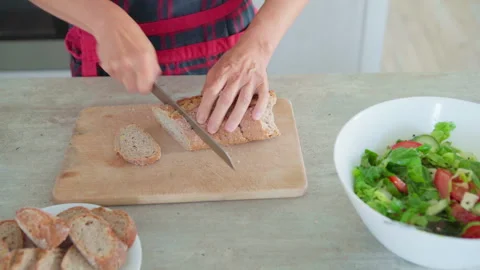 4K close-up video of woman’s hands cutting fresh baked bread in cozy kitchen, pr Video stock 320007264