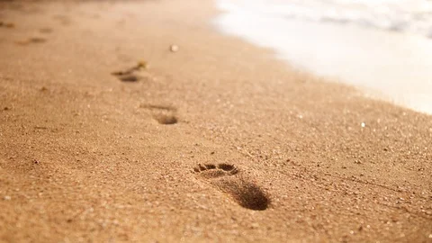 4k closeup video of sea waves wahing off footprints on the golden sand at beach Stock Footage