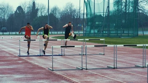 4K Competitive athletes running & jumping over hurdles at athletics track Stock Footage