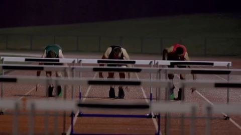 4K Competitive athletes running & jumping over hurdles at athletics track Stock Footage