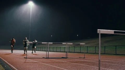 4K Competitive athletes running & jumping over hurdles at athletics track Stock Footage