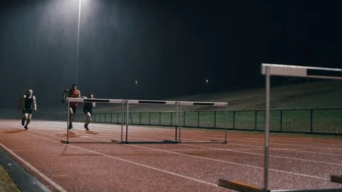 4K Competitive athletes running & jumping over hurdles at athletics track Stock Footage