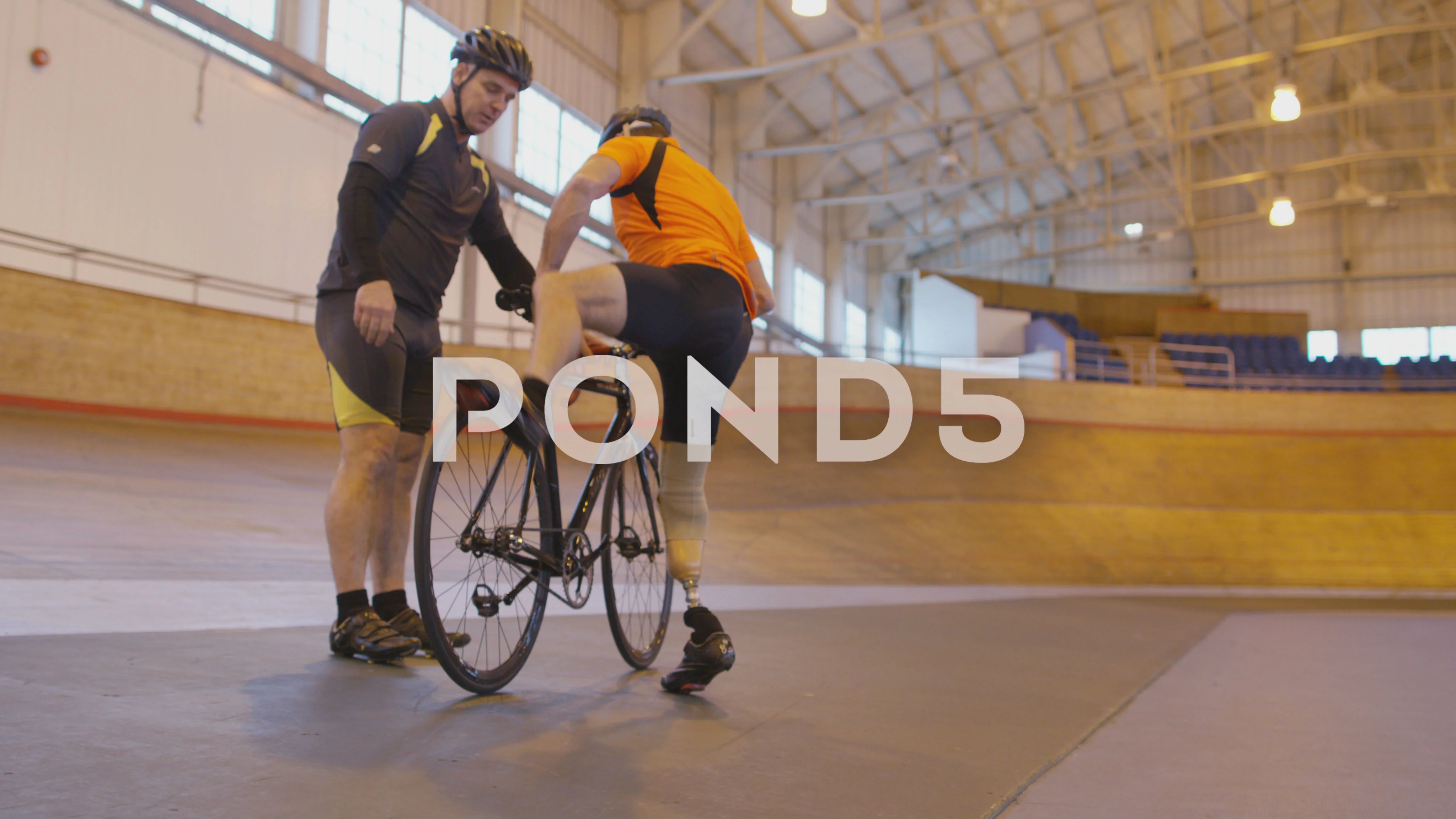 4K Competitive cyclist with prosthetic leg practicing with trainer in velodrome