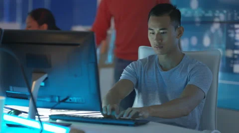 4K Computer game designer working at his desk with colleagues in background Stock Footage 67904360