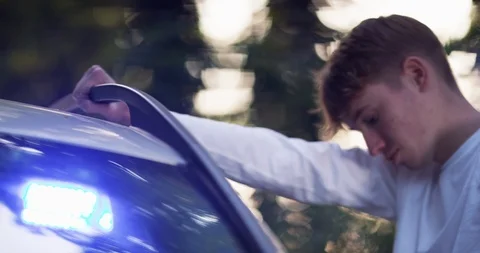 4K Cop handcuffing young man &amp; putting him in the back of the patrol car Stock Footage 113700850