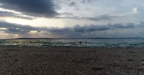 4K coral beach waves lapping with 2 female silhouettes swimming with cloudy s Stock Footage 81687071