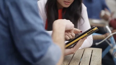 4K Couple Chatting &amp; Looking At Computer Tablet At Outdoor Cafe Table In City Stock Footage 75682531