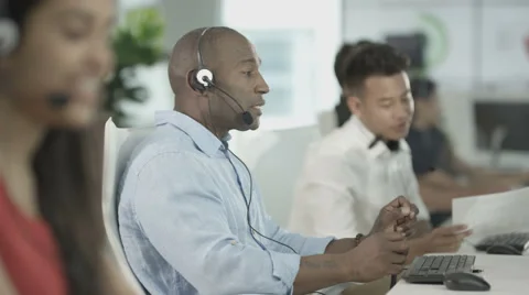4K Customer service ops taking calls in busy call center with manager overseeing Video stock 64579203