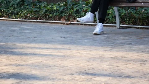 4k daylight static shot of a woman's feet with casual shoes seated on park bench Stock Footage 123434346