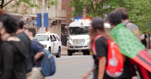 4K DEEP FOCUS SHOT OF FLASHING POLICE BUS WHILE PROTESTORS CROSS IN FRONT Stock Footage 132597425