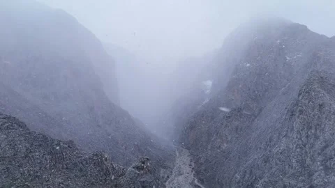 4K drone footage flying forward snowy mountain valley with snowfall and fog Stock Footage 336449603