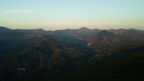 4K drone forward over forested mountains with scattered cities at sunset Stock Footage 315200930