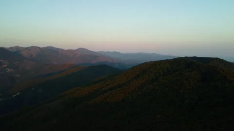 4K drone forward over forested mountains with mountain towns at sunset Stock Footage 315202714
