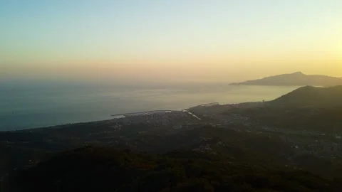 4K drone forward over seaside city and forested mountains at sunset Stock Footage 315206515