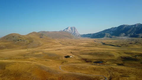 4K drone forward over yellow barren mountain valley with road, house, lake Stock Footage 315199222