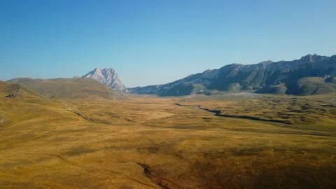 4K drone forward over yellow-orange barren valley with road and mountains Stock Footage 315205082