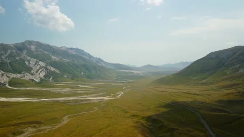 4K drone forward through green grassy mountain valley with road and mountains Stock Footage 315203667