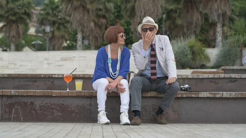 4K elderly couple having a cocktail on the beach, waving to some friends Stock Footage 90802673