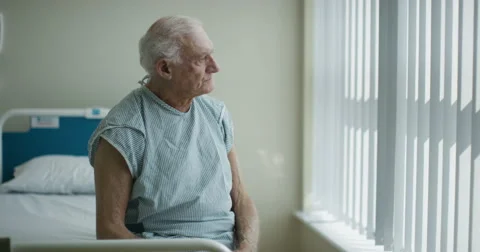 4K Elderly man sitting on bed in hospital room gets a visit from friendly nurse Stock Footage 63005498