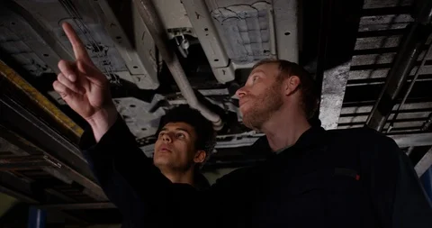 4K Experienced mechanic servicing vehicle with apprentice watching &amp; learning Stock Footage 112976018