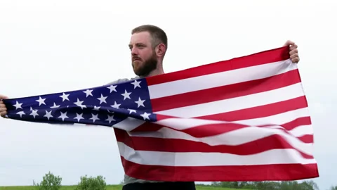 4k. Extremely serious bearded man holding in hands big American flag outdoors Stock Footage 154577361