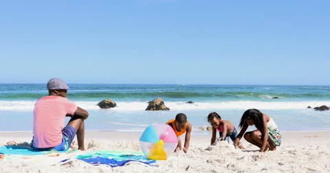4K Father relaxing while his children build a sand castle on beautiful beach Stock Footage 63929140