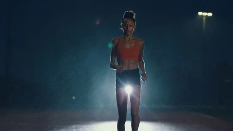 4K Female athlete training at running track in the dark & in the rain. Slowmo Stock Footage