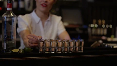 4K Female Bartender Setting Light To Row Of Shot Glasses Stock Footage 75631737