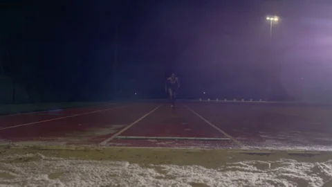 4K Female long jumper training at athletics track in the dark & rain. Slowmo Stock Footage
