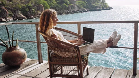 4k of Female working on laptop computer on balcony of bungalow. Successful blogg Stockbeeldmateriaal 199626880