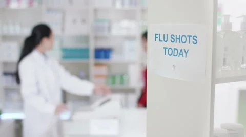 4K Flu shots notice in a chemist shop with worker serving customer in background Stock Footage