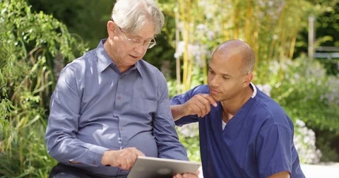 4K Friendly carer teaching senior man to use digital tablet in the garden Stock Footage 81223265
