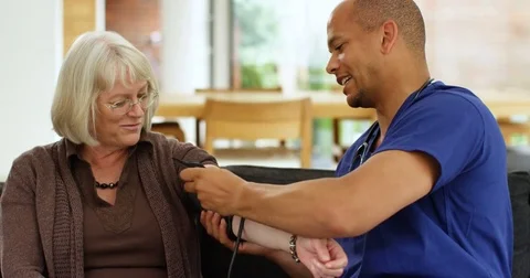 4K Friendly community nurse checking patient's blood pressure on home care visit Stock Footage 81196084