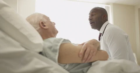 4K Friendly doctor comforting elderly patient at his bedside Stock Footage