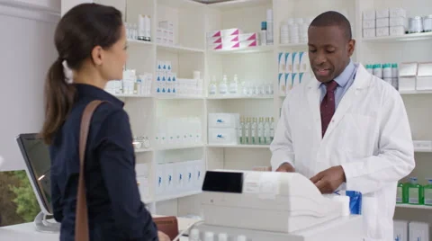 4K Friendly pharmacy worker serving customers &amp; taking payment at the till Stock Footage 67706519