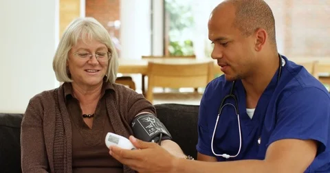 4K Friendly smiling doctor checking patient's blood pressure on home care visit Stock Footage 81195702