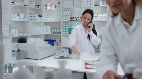 4K Friendly smiling pharmacy workers talking on phone &amp; stocking shelves Stock Footage 65023824