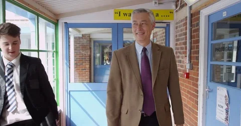 4K Friendly smiling teacher walking through school &amp; greeting young teen pupils Stock Footage 77284067