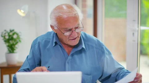 4K Frustrated senior man working on a laptop computer & looking at paperwork.  Stock Footage