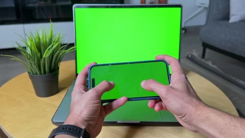 4K Green Screen Mockup of Hands Holding Smartphone in Front of Laptop Stock Footage 310546657