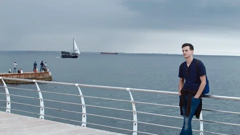4K A handsom man is standing on a pier. There could be seen the wavecutter and a 스톡 동영상 99932273