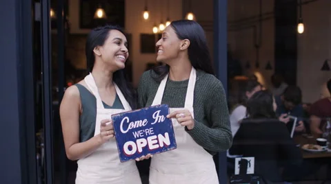 4K Happy women outside cafe hold up a sign to show they are open for business Stock Footage